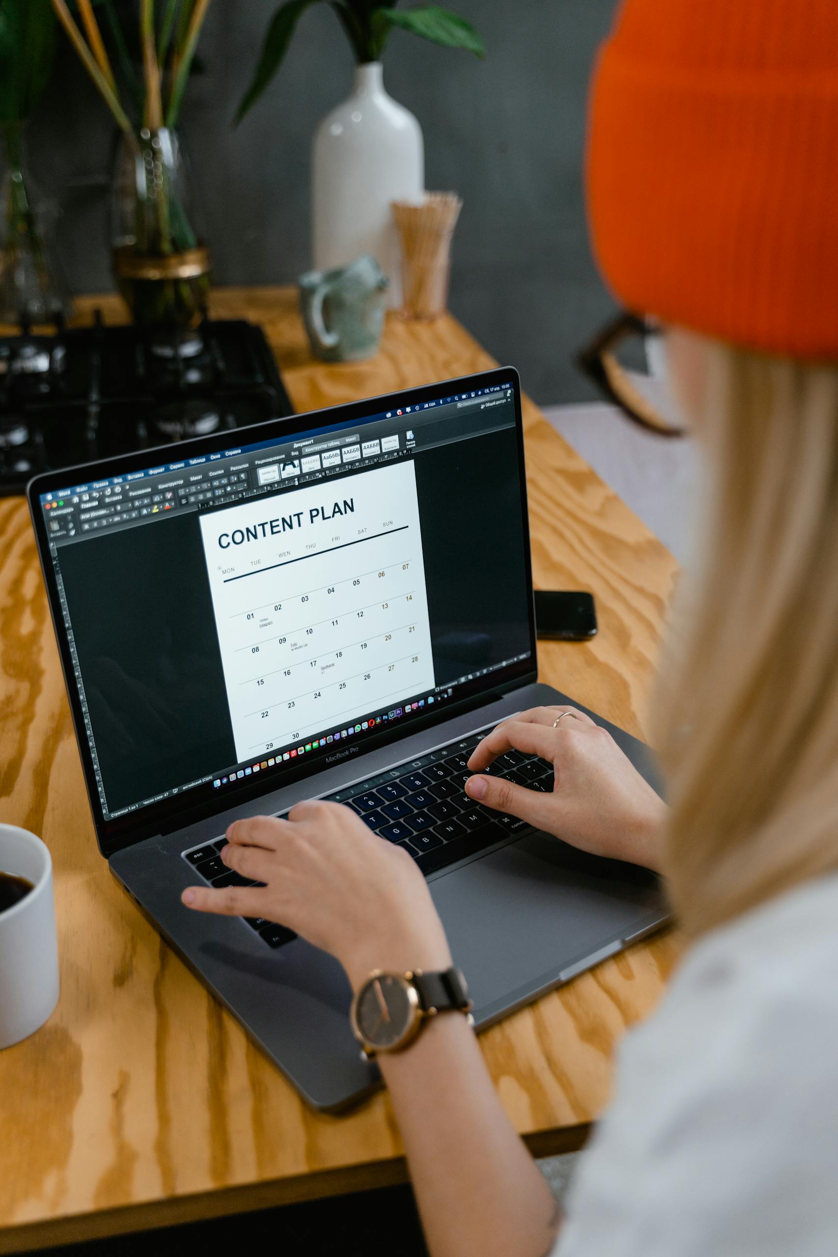 A woman working on a content plan using a laptop at a wooden table, showcasing productivity and planning.